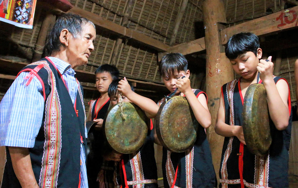 Già A Trang (bên trái) chỉ dạy cho các cháu cách đánh cồng chiêng truyền thống của người Xơ Đăng. Ảnh: NC.