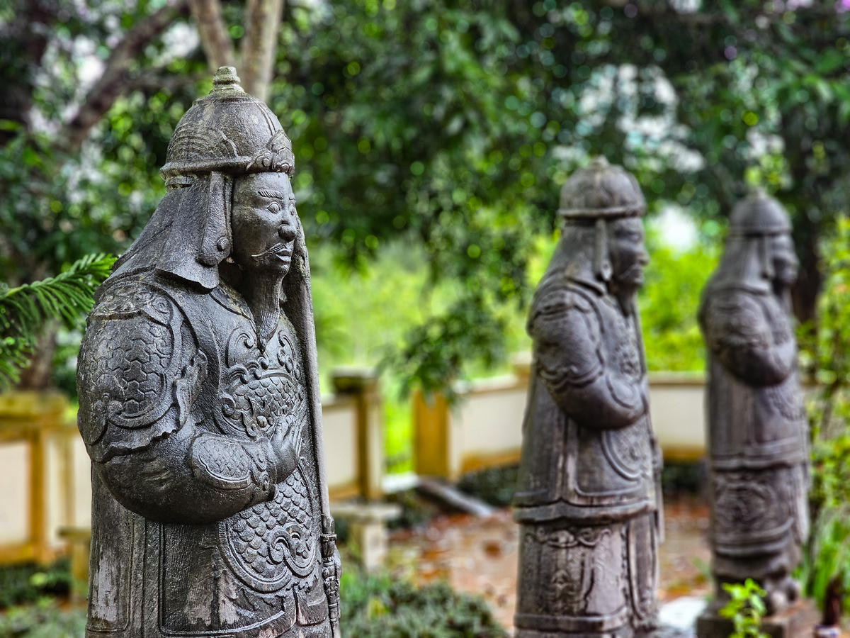 Các vũ sĩ mang trang phục võ quan thời chúa Trịnh, đầu đội mũ tròn có chóp, thân mặc giáp, tay bồng gươm. Gương mặt trang nghiêm, râu dài, các chi tiết trên mũ, áo giáp và trang phục được chạm khắc chắc khỏe, công phu. Ảnh: Đình Minh