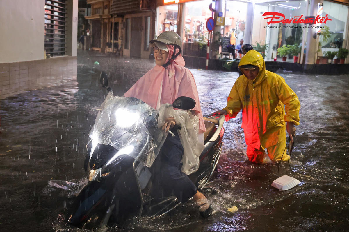 Công nhân thoát nước hỗ trợ đẩy xe máy cho người dân qua khu vực nước dềnh sau cơn mưa lớn.