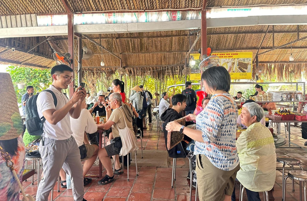 Du khách thích thú ghi lại khoảnh khắc trải nghiệm nuôi ong, thưởng thức mật ngọt giữa không gian miệt vườn Cồn Thới Sơn. (Ảnh: Thanh Lâm).