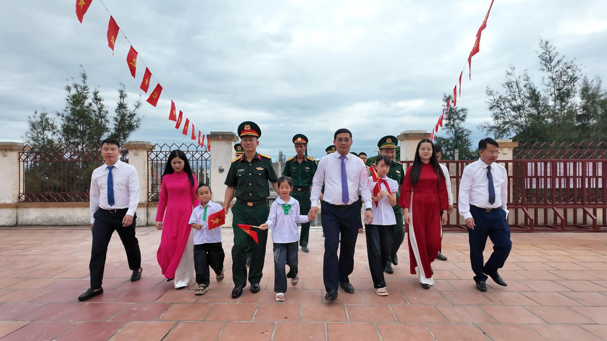 Các em học sinh ở đảo Trần được Chủ tịch UBND đặc khu Cô Tô Nguyễn Danh Hà cùng các thầy cô, cán bộ, chiến sĩ lực lượng vũ trang đang công tác trên đảo dắt tay vào trường.