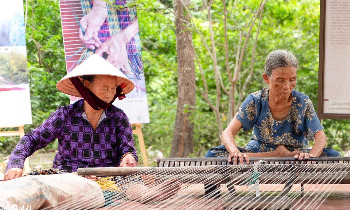 Bà Trần Thị Mai (đội nón lá) đang ngồi dệt chiếu ở làng Thạch Tân. Ảnh: HĐ.