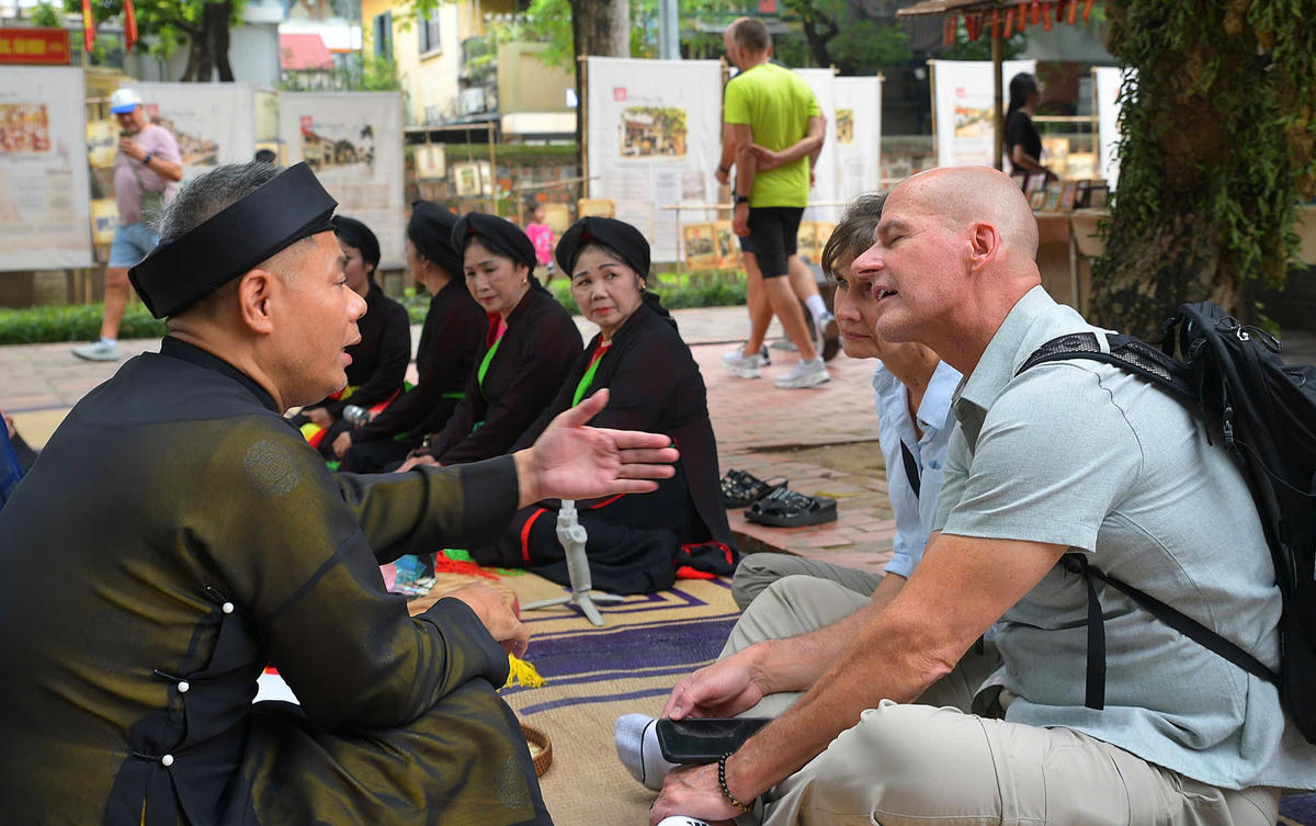 Du khách quốc tế trò chuyện cùng liền anh, liền chị, tìm hiểu những làn điệu Quan họ tại không gian trưng bày. 