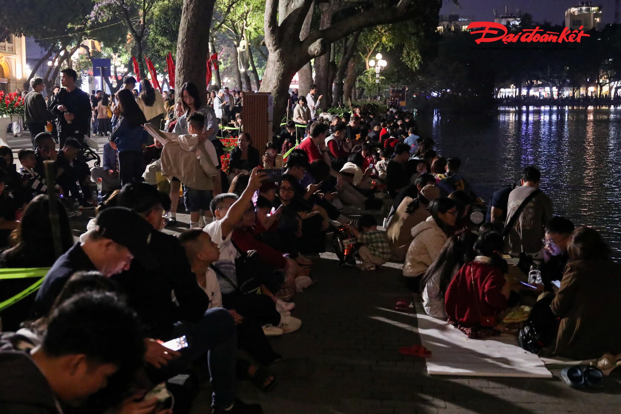 Ven hồ Hoàn Kiếm, người dân tìm cho mình những chỗ ngồi thuận lợi để có thể quan sát trọn vẹn màn trình diễn ánh sáng trên bầu trời. Nhiều nhóm bạn trẻ tranh thủ ghi lại khoảnh khắc cuối cùng của năm cũ, trong khi các gia đình quây quần bên nhau, cùng chờ đợi giây phút chuyển giao. Không khí vui tươi, rộn ràng lan tỏa khắp không gian trung tâm Thủ đô.