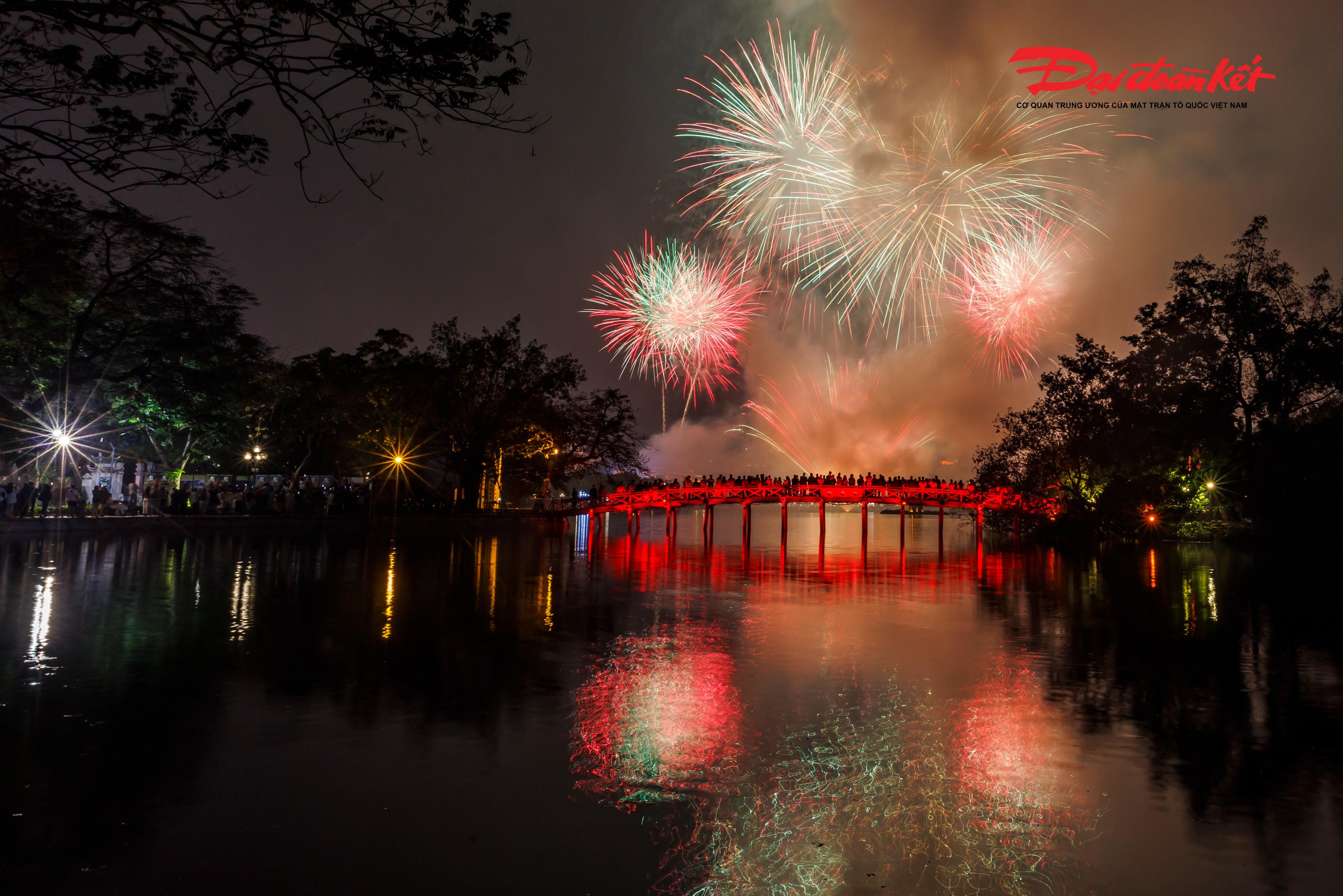 Những chùm pháo hoa đủ sắc đỏ, vàng, xanh, tím liên tiếp bung nở, phản chiếu lung linh xuống mặt nước phẳng lặng của hồ, tạo nên khung cảnh huyền ảo. Tiếng reo hò, tiếng vỗ tay hòa cùng tiếng nổ rộn ràng làm không khí thêm phần náo nhiệt.
