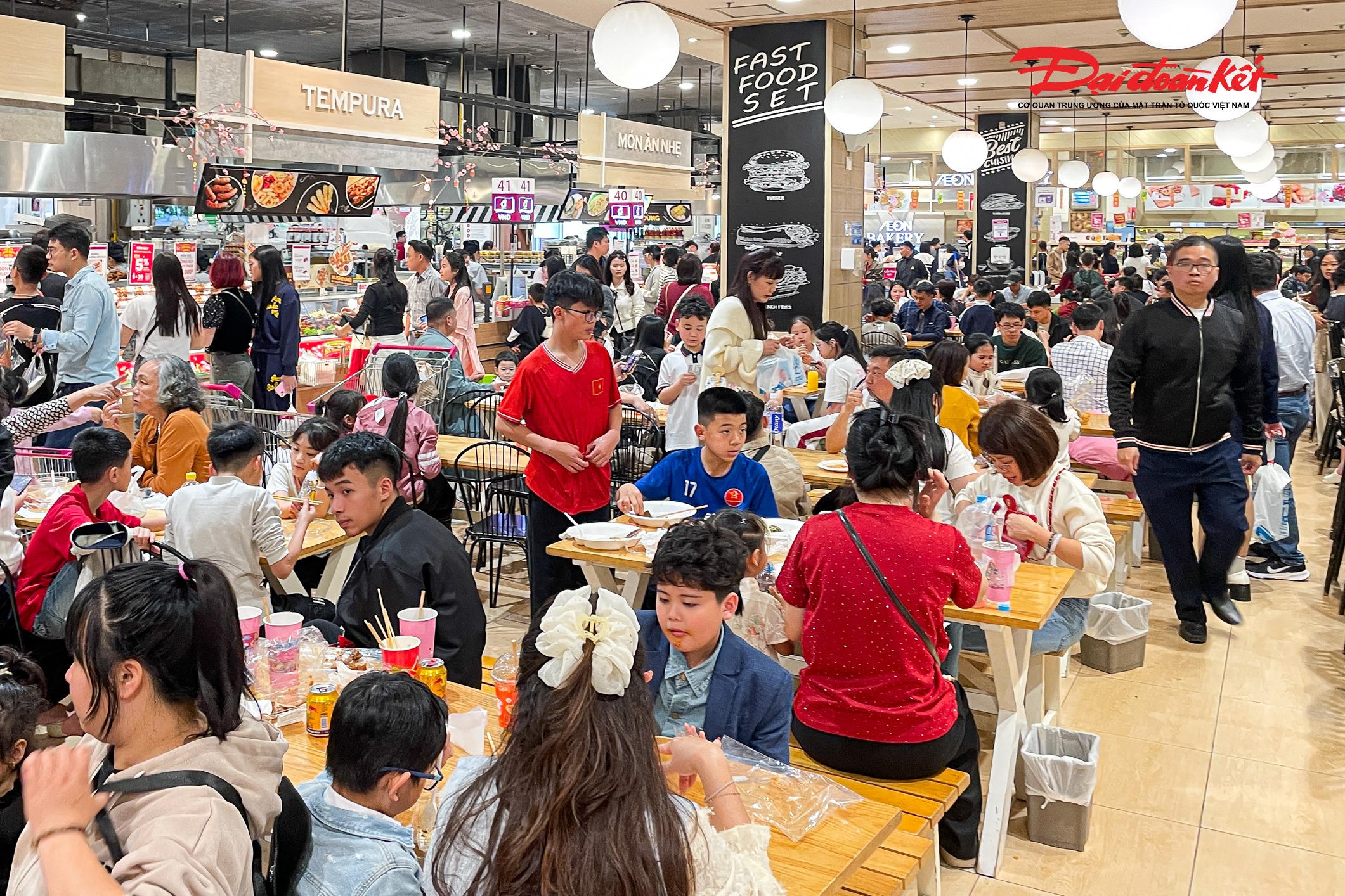 Ghi nhận vào khung giờ trưa và đầu giờ chiều, hầu hết các nhà hàng, quán ăn tại một trung tâm thương mại ở Long Biên (Hà Nội) đều kín bàn. Nhiều gia đình phải xếp hàng chờ từ 20–40 phút mới đến lượt. Khu vực lấy số thứ tự luôn đông nghịt người, trong khi nhân viên liên tục tất bật hướng dẫn khách, sắp xếp chỗ ngồi và phục vụ món ăn.