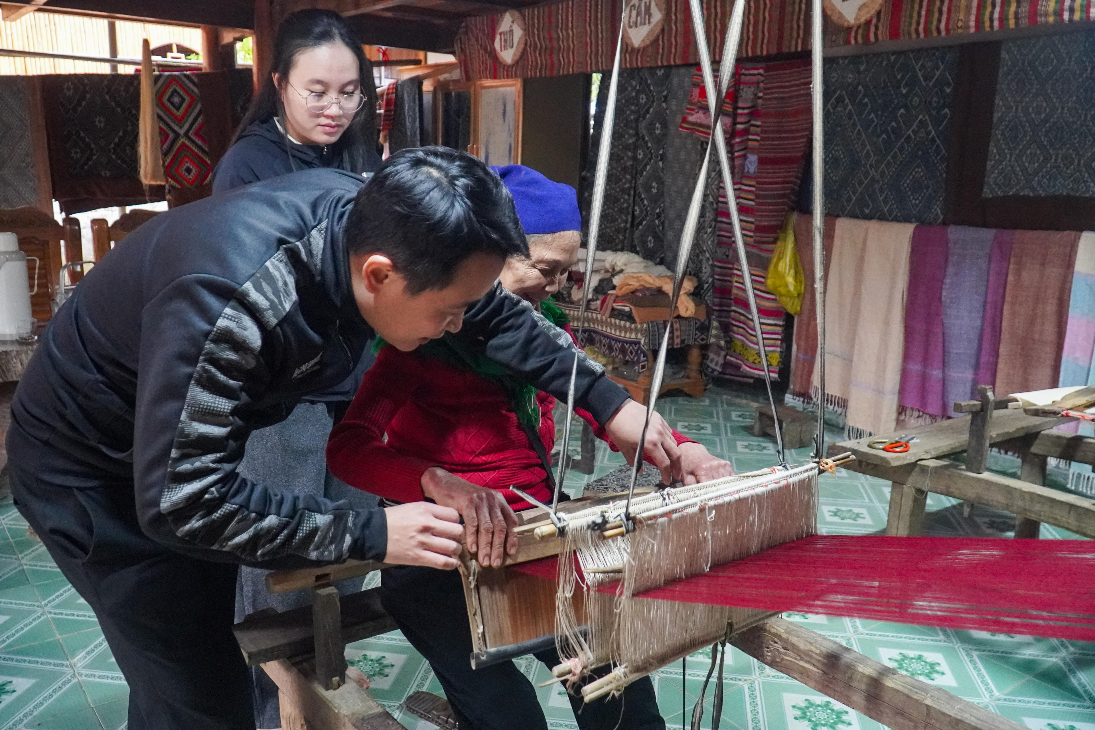 Không chỉ tham quan, nhiều người còn trực tiếp trải nghiệm dệt vải, nghe các nghệ nhân kể chuyện về nghề và chọn mua những sản phẩm như khăn, túi xách, vỏ gối, tấm phủ… làm quà lưu niệm. Ảnh: Đình Minh.